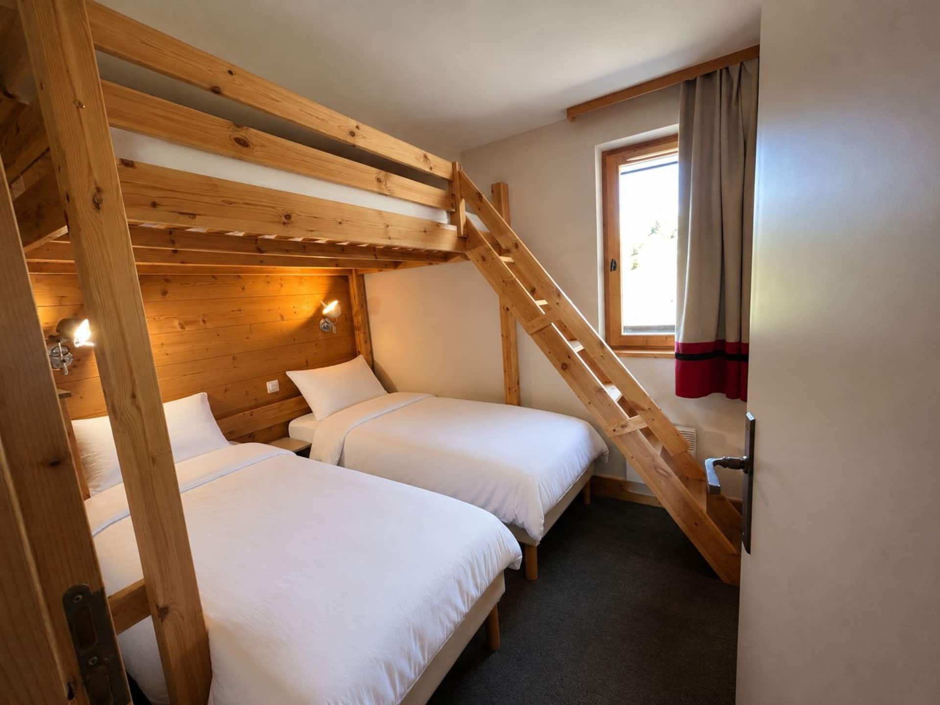 Chambre en lambris avec deux lits simples et une mezzanine accessible par une échelle